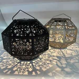 May include: Two decorative metal lanterns with intricate cut-out designs. The lantern on the left is black and the lantern on the right is silver.