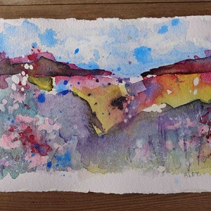 May include: Watercolor landscape painting with a colorful abstract design. The artwork features a mountain range in shades of red and brown, with a sky of blue and white. The foreground has pink, yellow, and purple hues. Signed "ALEY".