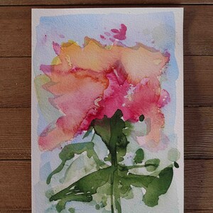 May include: Watercolor painting of a flower in shades of pink, orange, and green. The artwork features a loose, expressive style with visible brushstrokes and a light blue background. The artist's signature, "ALEY," is in the lower right corner.