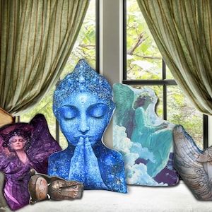 May include: A selection of decorative art pieces, including a blue Buddha head, a purple figure, a wooden box, and two angel-themed artworks. The items are displayed on a white surface, with a window and curtains in the background.