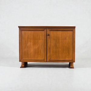 Può includere: Un mobile in legno a due ante, con finitura marrone scuro. Il mobile ha una forma rettangolare con un piano piatto e poggia su quattro gambe corte. Le ante presentano un semplice design a pannelli e una piccola maniglia rotonda. Il mobile è largo circa 90 cm.