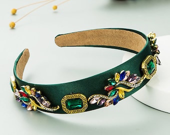 May include: A green headband with a gold and jewel embellishment. The headband is decorated with colorful rhinestones and a large green gemstone.