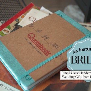 May include: A brown leather bound journal with a teal ribbon bookmark. The journal has the words 'Quotebook' and 'Live it. Remember it. Quote it.' printed on the front cover. The journal has a sticker that says 'As featured on BRIDES.com' and 'The 34 Best Handcrafted and Unique Wedding Gifts from Etsy in 2022'.