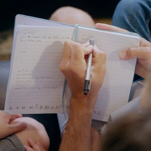 Puede incluir: Una persona escribiendo en un cuaderno de l&iacute;neas con un bol&iacute;grafo plateado. El cuaderno est&aacute; abierto y la persona lo sostiene con su mano izquierda. La mano derecha de la persona sostiene el bol&iacute;grafo y escribe en la p&aacute;gina. El cuaderno tiene una cubierta azul y est&aacute; sentado en el regazo de una persona.