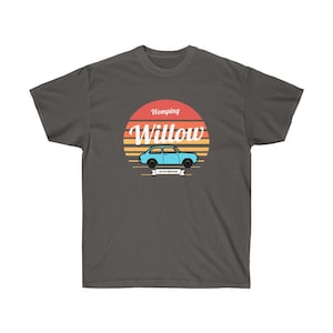 May include: A dark gray t-shirt with a retro-style graphic of a blue car in front of a sunset with the text "Womping Willow Auto Repair" in white.