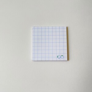 May include: A white notepad with blue grid lines and a small green drawing of two blueberries on the bottom right corner.