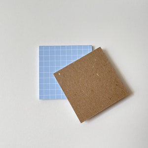 May include: Two square sticky notes, one blue with a grid pattern and one brown with a rough texture.