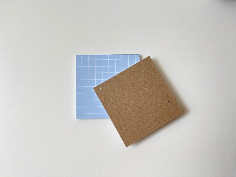 May include: Two square sticky notes, one blue with a grid pattern and one brown with a rough texture.