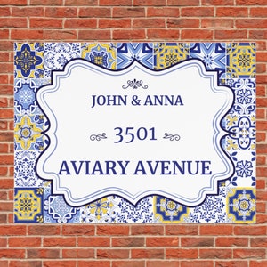 May include: A white sign with a blue and yellow patterned border. The sign has a decorative border and says "John & Anna 3501 Aviary Avenue".