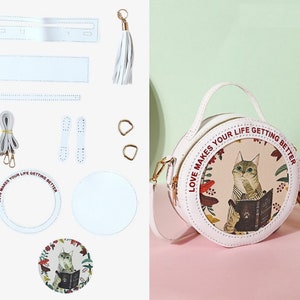 May include: A white leather DIY round bag kit with a cat and floral print design. The kit includes the bag pieces, a strap, two handles, two metal rings, a tassel, and a printed design for the bag. The bag has the text 'Love Makes Your Life Getting Better' around the design.