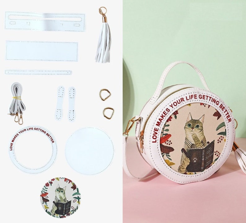 May include: A white leather DIY round bag kit with a cat and floral print design. The kit includes the bag pieces, a strap, two handles, two metal rings, a tassel, and a printed design for the bag. The bag has the text 'Love Makes Your Life Getting Better' around the design.