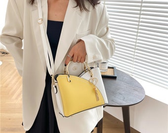 May include: A yellow and white handbag with a gold handle and a heart-shaped charm. The bag has a top flap and a short strap.