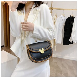 May include: A black faux leather shoulder bag with a brown stitched trim and a gold Mickey Mouse shaped clasp. The bag has a chain strap.