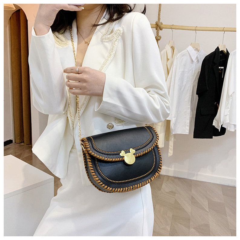 May include: A black faux leather shoulder bag with a brown stitched trim and a gold Mickey Mouse shaped clasp. The bag has a chain strap.