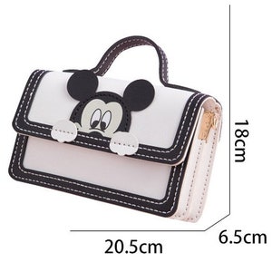 以下が含まれることがあります： ミッキーマウスのキャラクターデザインが施された白黒のハンドバッグ。ハンドバッグはトップハンドルが付いており、6.5cm x 20.5cm x 18cmです。