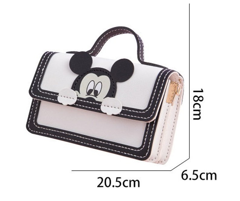 以下が含まれることがあります： ミッキーマウスのキャラクターデザインが施された白黒のハンドバッグ。ハンドバッグはトップハンドルが付いており、6.5cm x 20.5cm x 18cmです。
