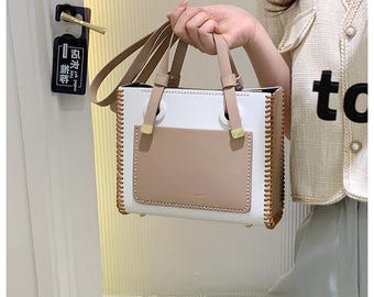 May include: A white and beige tote bag with a stitched design and gold accents. The bag has a top handle and a flap closure.