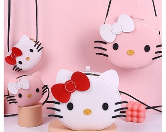 May include: Three pink and white Hello Kitty purses with black eyes and whiskers. The purses have red bows and are made of faux leather. The purses are hanging from black straps.