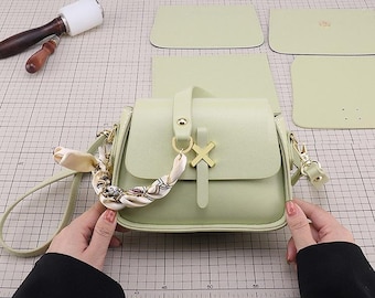 May include: A light green leather satchel bag with a gold clasp and a decorative scarf. The bag has a long strap and a shorter handle.