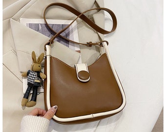 May include: A brown leather shoulder bag with a white trim. The bag has a flap closure with a button.