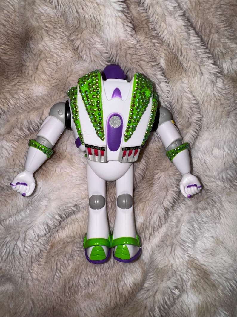 Pode incluir: Um brinquedo rob&ocirc; branco e verde com detalhes em roxo. O rob&ocirc; tem pedras preciosas verdes nas costas e nos bra&ccedil;os. Os p&eacute;s do rob&ocirc; s&atilde;o verdes e roxos. Os bra&ccedil;os do rob&ocirc; est&atilde;o estendidos. A palavra "DANGER" &eacute; vis&iacute;vel nas costas do rob&ocirc;.