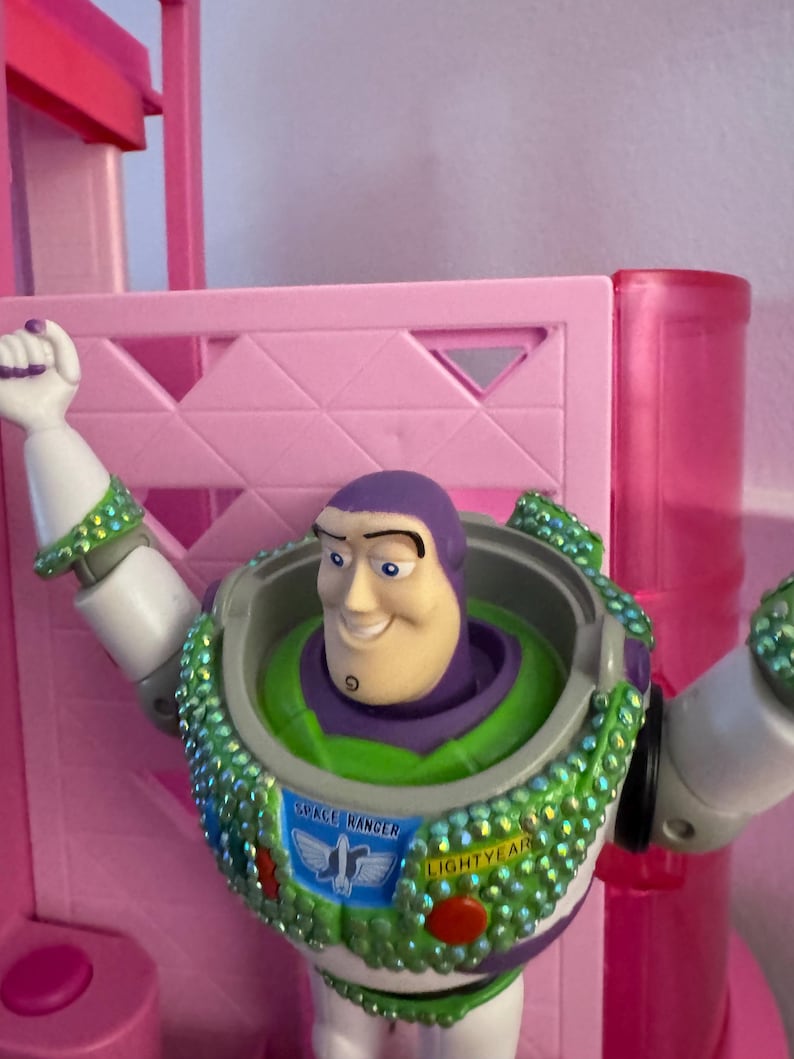 Pode incluir: Figura de a&ccedil;&atilde;o do Buzz Lightyear com um traje espacial verde e branco, cabe&ccedil;a roxa e express&atilde;o sorridente. As palavras "SPACE RANGER" e "LIGHTYEAR" est&atilde;o no peito. O fundo &eacute; rosa.