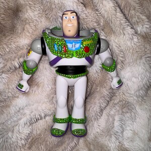 Pode incluir: Figura de a&ccedil;&atilde;o do Buzz Lightyear, com um design de fato espacial branco e roxo com detalhes verdes e prateados. A figura tem um rosto sorridente e as palavras "Space Ranger" e "Lightyear" s&atilde;o vis&iacute;veis no peito.