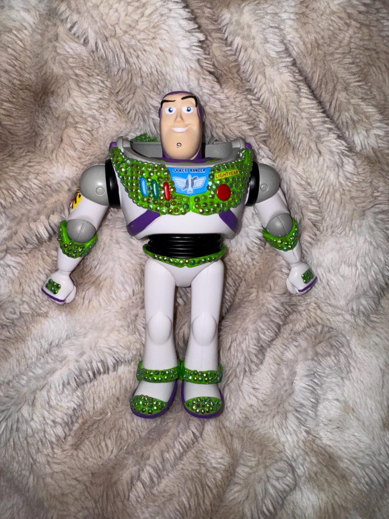 Pode incluir: Figura de a&ccedil;&atilde;o do Buzz Lightyear, com um design de fato espacial branco e roxo com detalhes verdes e prateados. A figura tem um rosto sorridente e as palavras "Space Ranger" e "Lightyear" s&atilde;o vis&iacute;veis no peito.