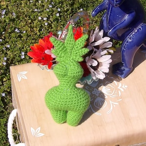 May include: A wooden box with a white floral design, a green crocheted figure, and a blue ceramic dinosaur figurine. The box is open and the dinosaur is standing on the edge of the box.