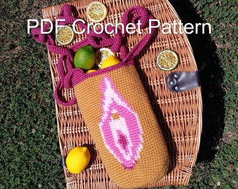 May include: A crocheted bag with a pink and white design on a brown background. The bag has a pink strap and is sitting on a wicker basket with lemons and limes.