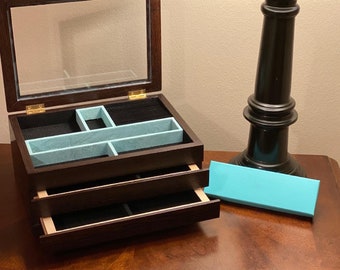 May include: A dark brown wooden jewelry box with a glass top and two drawers. The box has a light blue velvet interior and is open to reveal the compartments.