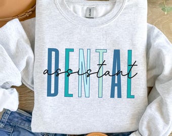 May include: A gray sweatshirt with the text "DENTAL assistant" in blue, green, and white lettering. The text is in a stylized font with a gradient effect.