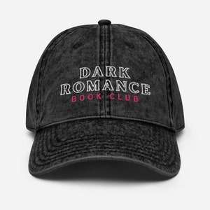Może przedstawiać: Czarna, zniszczona bejsbolówka z denimu z białym haftem z napisem "DARK ROMANCE BOOK CLUB", przy czym słowo "ROMANCE" jest różowe.