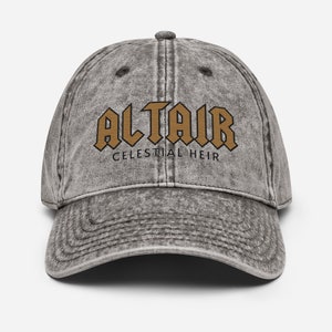 May include: A grey distressed denim baseball cap with the text "Altair Celestial Heir" in brown embroidered letters.