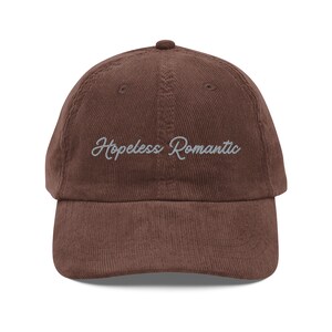 May include: A brown corduroy baseball cap with the text "Hopeless Romantic" embroidered in white on the front.