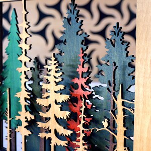 May include: A wooden wall art piece featuring a layered forest scene with trees in shades of green, brown, and red. The trees are cut out and layered to create a 3D effect.