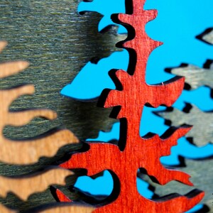 May include: Close-up of a wooden Christmas tree ornament with a red, brown, and green color scheme. The ornament is cut out in the shape of a tree and has a rustic, hand-crafted look.
