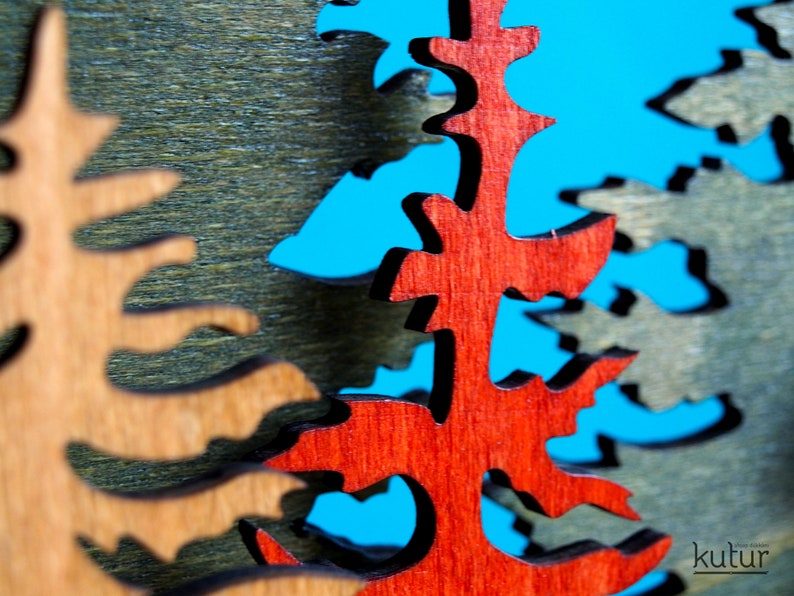May include: Close-up of a wooden Christmas tree ornament with a red, brown, and green color scheme. The ornament is cut out in the shape of a tree and has a rustic, hand-crafted look.
