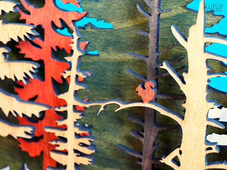 May include: A wooden wall art piece depicting a forest scene with a red bird perched on a branch. The trees are cut out of wood and painted in shades of brown, green, and red.