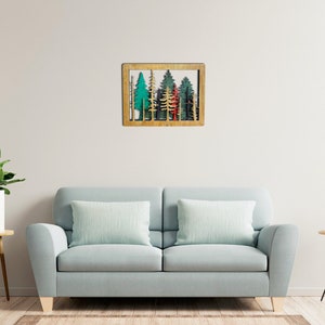 May include: A wooden wall decor featuring a framed cutout of a forest scene with green, blue, and red trees. The frame is a light brown wood.