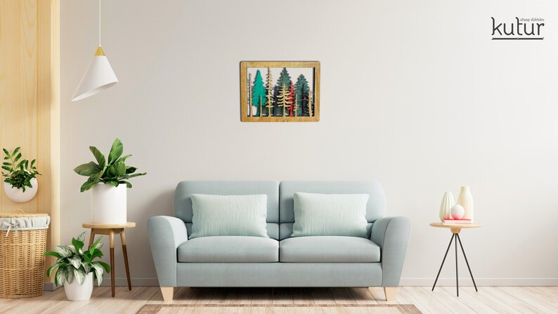 May include: A wooden wall decor featuring a framed cutout of a forest scene with green, blue, and red trees. The frame is a light brown wood.
