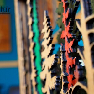 May include: Close-up of a wooden wall art piece with a layered design of trees in shades of green, red, and brown. The trees are cut out of the wood and layered to create a 3D effect.