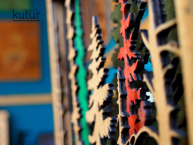 May include: Close-up of a wooden wall art piece with a layered design of trees in shades of green, red, and brown. The trees are cut out of the wood and layered to create a 3D effect.