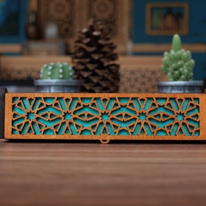 Op de afbeelding: Een houten doos met een turquoise geometrisch patroon dat in de voorkant is gegraveerd. De doos is gemaakt van donker hout en heeft een natuurlijke houtkleur.