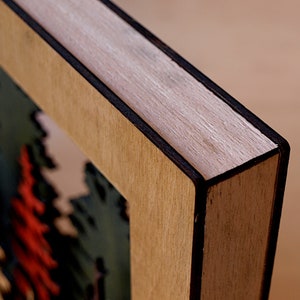 May include: Close-up of a wooden frame with a black border. The frame is made of light wood with a natural grain. The frame is empty, but there is a hint of a colorful image inside.