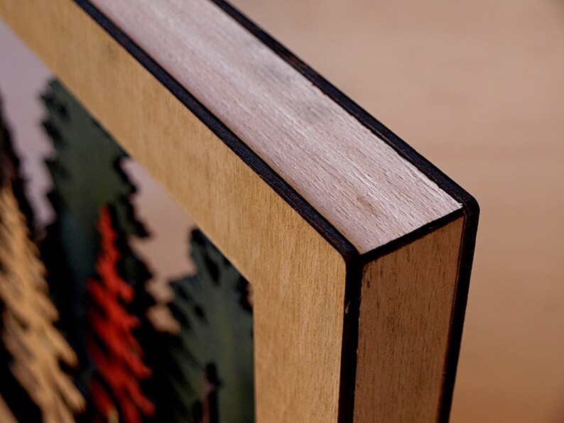 May include: Close-up of a wooden frame with a black border. The frame is made of light wood with a natural grain. The frame is empty, but there is a hint of a colorful image inside.