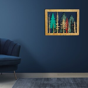 May include: A wooden wall decor featuring a cutout design of a forest with trees in shades of green, red, and blue. The decor is mounted on a blue wall.