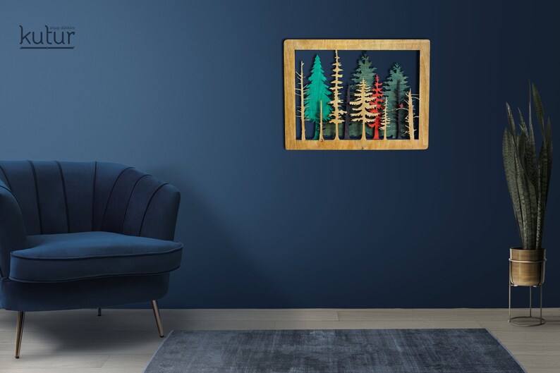 May include: A wooden wall decor featuring a cutout design of a forest with trees in shades of green, red, and blue. The decor is mounted on a blue wall.