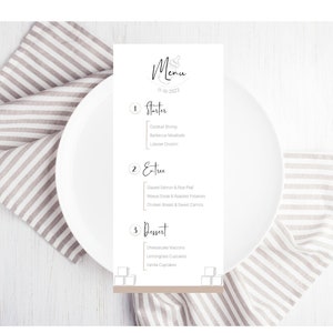 May include: A white menu card with a black and white illustration of a bottle and the word "Menu" printed on it. The menu lists "Starter", "Entree", and "Dessert" with a few food items under each category. The card is on a white surface with a gray and white striped napkin.