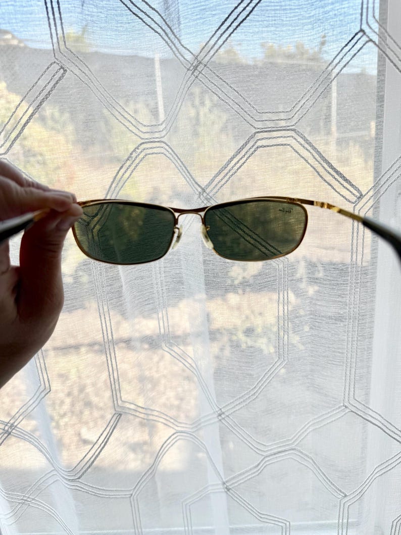 Peut inclure: Lunettes de soleil &agrave; monture en m&eacute;tal dor&eacute; dot&eacute;es de verres rectangulaires vert fonc&eacute;. Le verre droit pr&eacute;sente un petit logo blanc. La fine monture m&eacute;tallique comprend des plaquettes r&eacute;glables et des branches fines aux extr&eacute;mit&eacute;s sombres.
